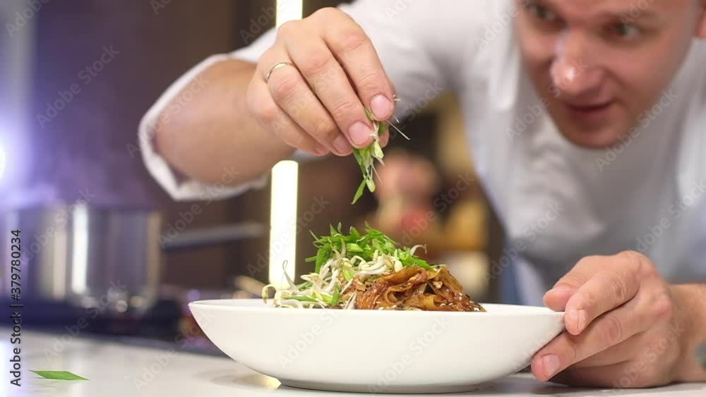 Young professional chef in the kitchen prepares Italian pasta. A man decorates a dish on a plate with green herbs. Delicious gourmet lunch prepared in the home kitchen. Young professional chef in the kitchen prepares Italian pasta. A man decorates a dish on a plate with green herbs. Delicious gourmet lunch prepared in the home kitchen.
