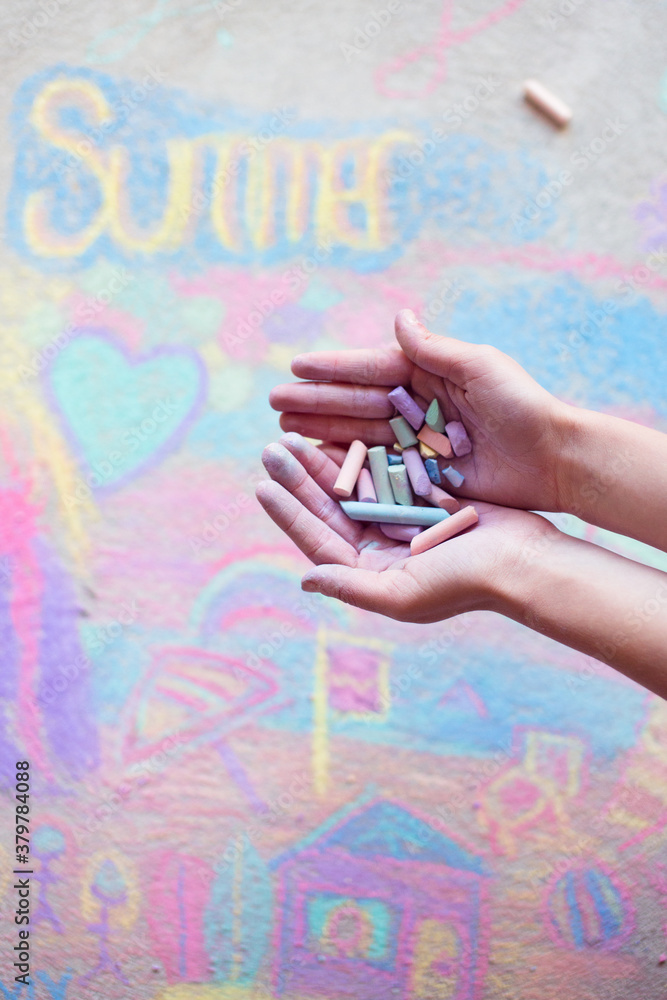 A handful of chalk held above a colourful pavement chalk drawing A handful of chalk held above a colourful pavement chalk drawing