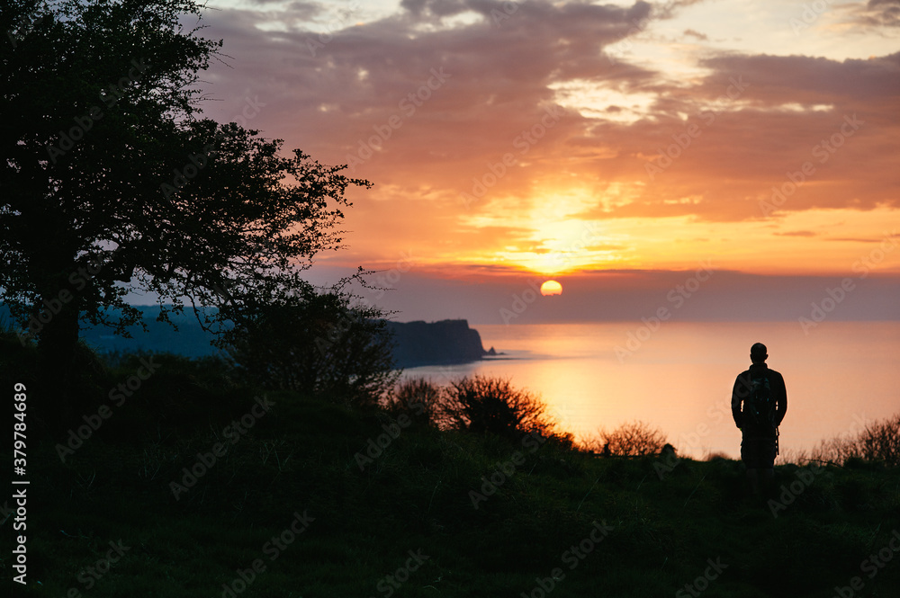 Man standing on cliff watching the sunset over the sea Man standing on cliff watching the sunset over the sea