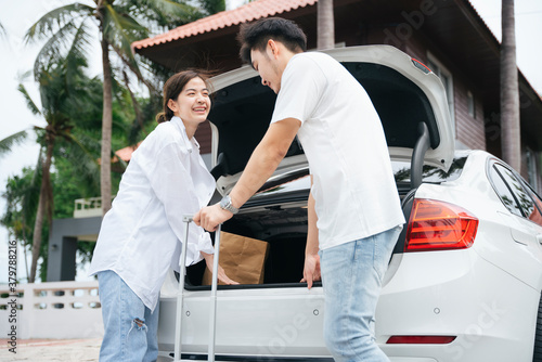 Asian couple prepare for a road trip putting luggage case in car trunk.