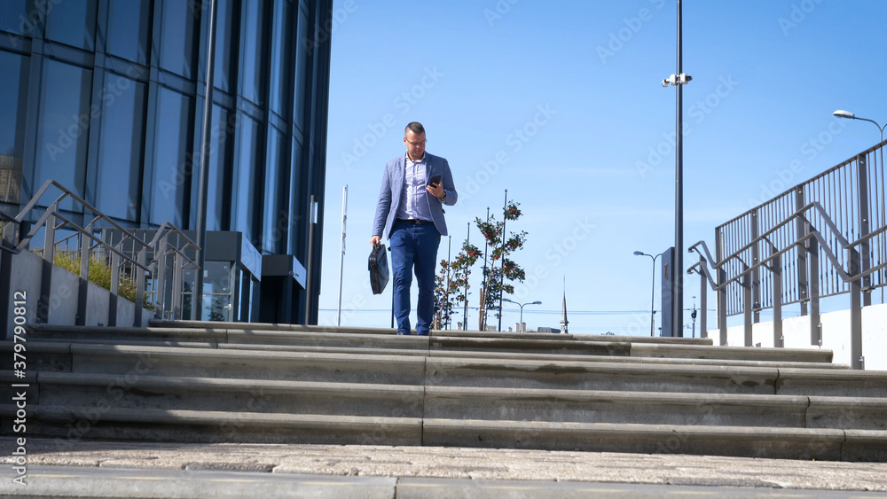 Celebrating success. Low angle view of excited young businessman keeping arms raised and expressing positivity while standing outdoors with office building in the background