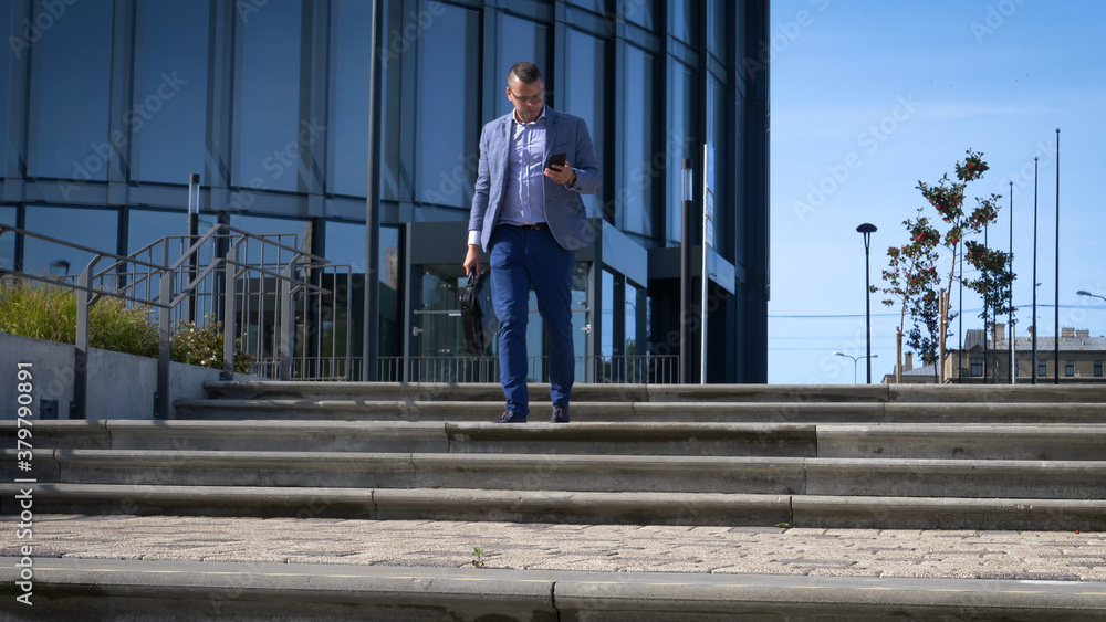 Celebrating success. Low angle view of excited young businessman keeping arms raised and expressing positivity while standing outdoors with office building in the background Celebrating success. Low angle view of excited young businessman keeping arms raised and expressing positivity while standing outdoors with office building in the background