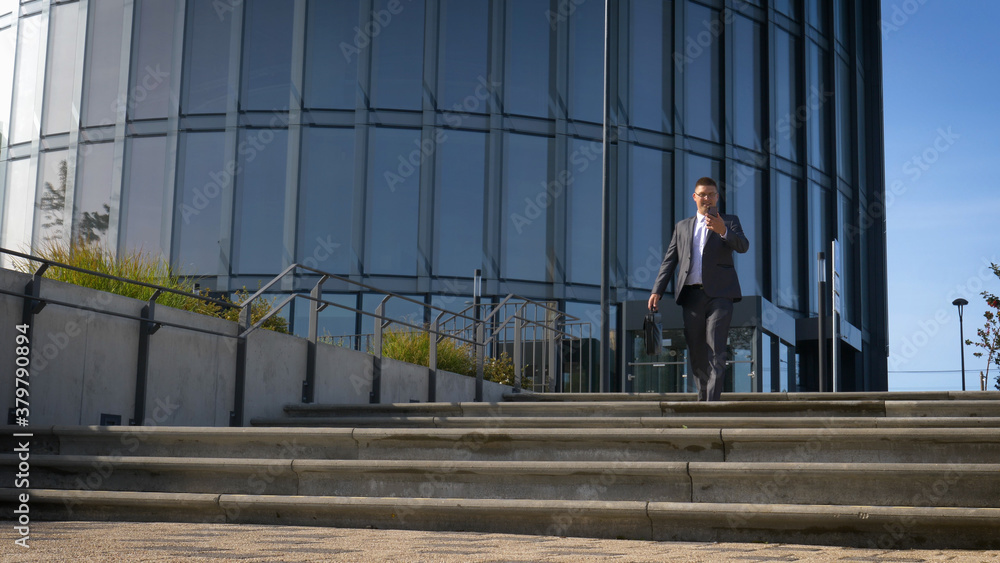 Celebrating success. Low angle view of excited young businessman keeping arms raised and expressing positivity while standing outdoors with office building in the background Celebrating success. Low angle view of excited young businessman keeping arms raised and expressing positivity while standing outdoors with office building in the background