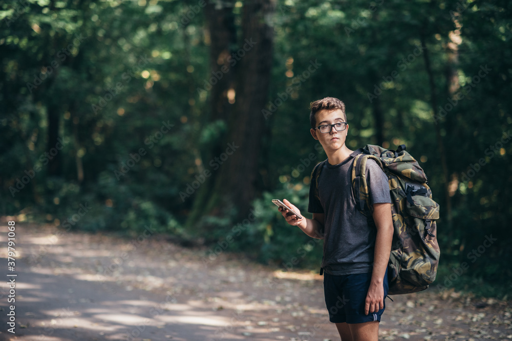 Young teen boy with a backpack exploring the forest, and using smartphone Young teen boy with a backpack exploring the forest, and using smartphone