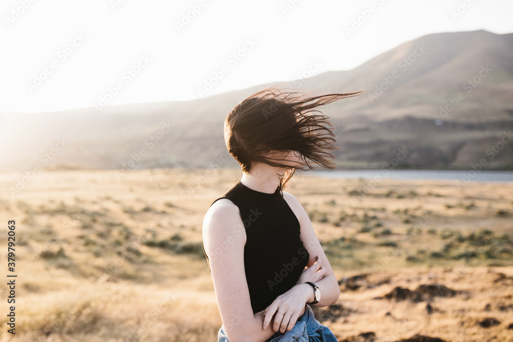 woman standing in field with wind blowing hair over face woman standing in field with wind blowing hair over face