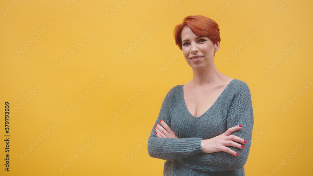 Obraz premium Portrait of redhead middle aged woman with crosed hands smilling, isolated on the orange background. High quality photo