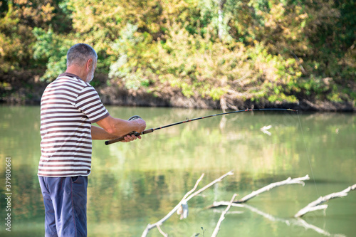 retired man with white beard pulling the rod with old style round reel on the autumn river