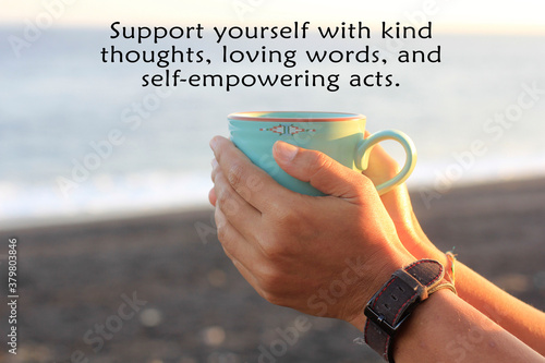 Inspirational motivational quote - Support yourself with kind thoughts, loving words, and self empowering acts. With background of person hands holding a cup of coffee on the beach at sunset sunrise. photo