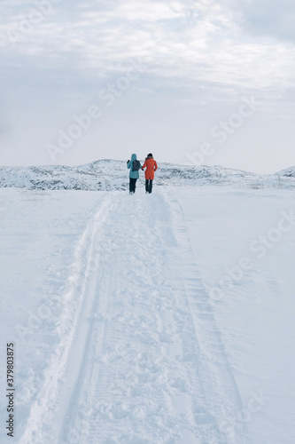 two girls in bright jackets walk along a white snowy road through the tundra beyond the Arctic Circle on a frosty clear day