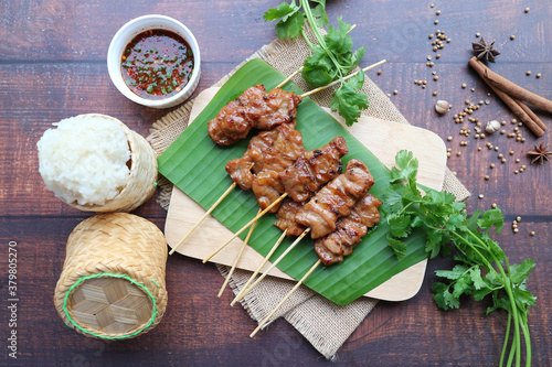 Grilled pork skewer with sticky rice  - Thai bbq pork served on the wooden tray with sticky rice and spicy dipping sauce ( Khao Neaow Moo Ping) Top view photo