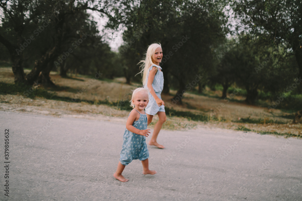 Two little sisters running along the road and looking into the camera Two little sisters running along the road and looking into the camera