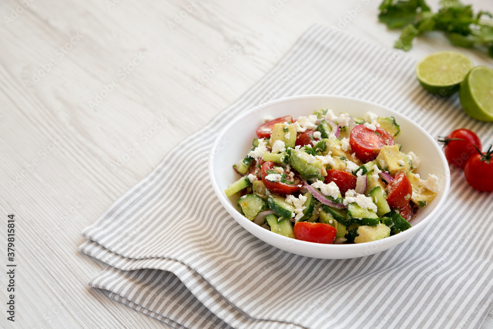 Delicious Avocado Tomato and Cucumber Salad in a bowl on a white wooden background, side view. Copy space. Delicious Avocado Tomato and Cucumber Salad in a bowl on a white wooden background, side view. Copy space.