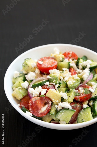 Delicious Avocado Tomato and Cucumber Salad in a white bowl on a black background, low angle view. Copy space.