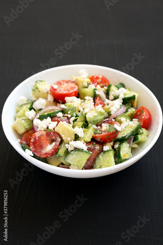 Delicious Avocado Tomato and Cucumber Salad in a white bowl on a black surface, low angle view.