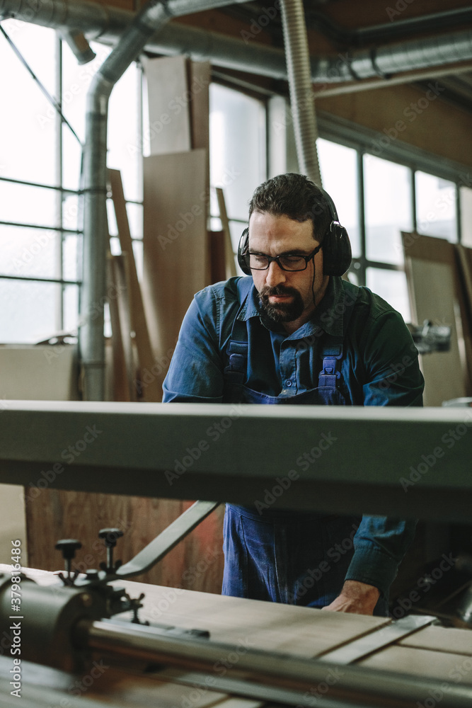 portrait of a bearded woodworker with black protection earmuffs working on a belt sander portrait of a bearded woodworker with black protection earmuffs working on a belt sander