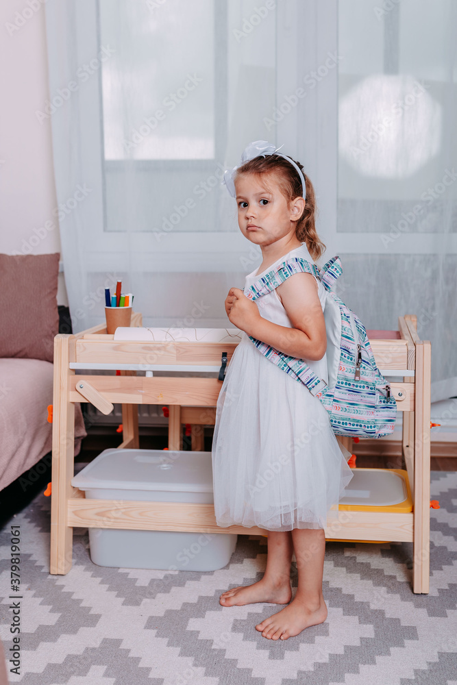 Little student with blue backpack near school desk. Back to school. Little girl studies at home. Little student with blue backpack near school desk. Back to school. Little girl studies at home.