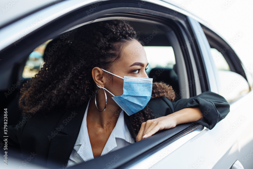 Young business woman looks out of a window of her personal car during pandemic covid-19. Business trips during pandemic, new normal and coronavirus travel safety concept.