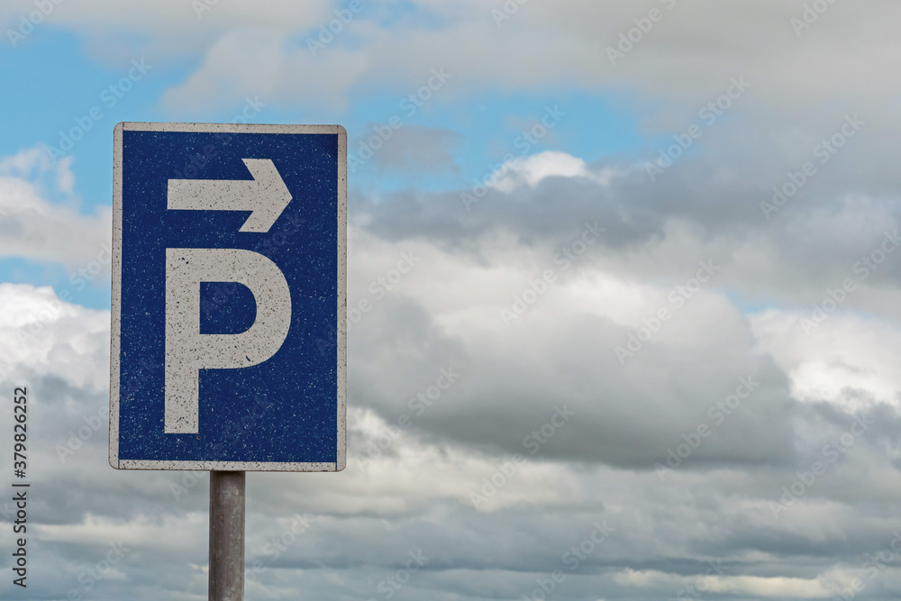 Blue and white parking sign with direction to the right arrow, cloudy sky in the background. Blue and white parking sign with direction to the right arrow, cloudy sky in the background.