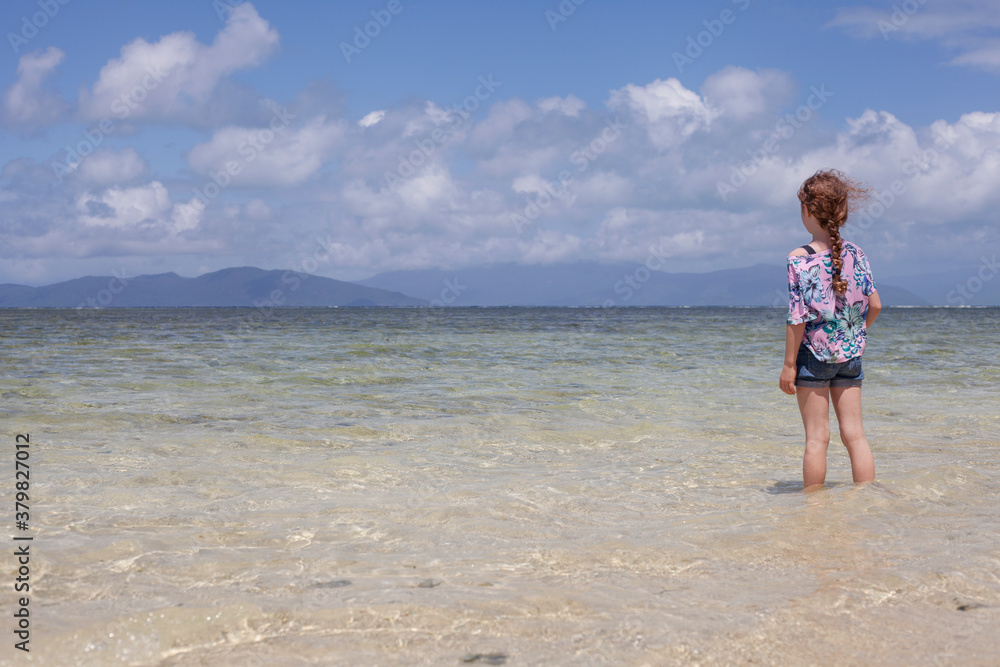 Girl standing in water looking out to beautiful island Girl standing in water looking out to beautiful island