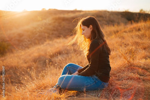 Photo of young woman meditating outdoor at sunset during autumn time