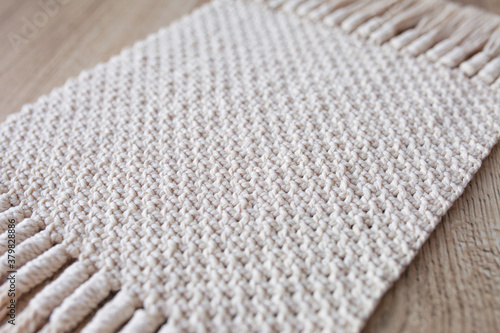 Handmade beige macrame pattern background. Macrame texture, ECO friendly, modern knitting. Macrame rug on wooden table