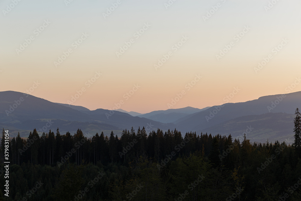 Landscape with mountains at sunset. Orange Sun setting behind the Mountains. Colorful sunrise over the Carpathian Mountains.
