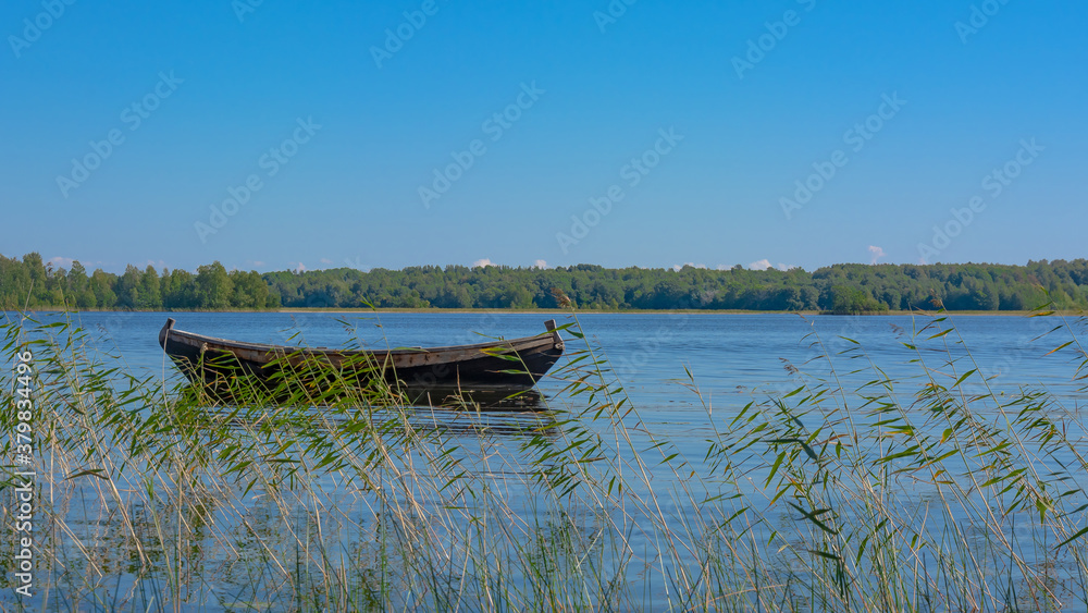 Landscape on the Kizhi island in Lake Onega on a summer sunny day. Lonely wooden fishing boat on the lake, among the aquatic vegetation. In the distance, the opposite shore of the lake Landscape on the Kizhi island in Lake Onega on a summer sunny day. Lonely wooden fishing boat on the lake, among the aquatic vegetation. In the distance, the opposite shore of the lake