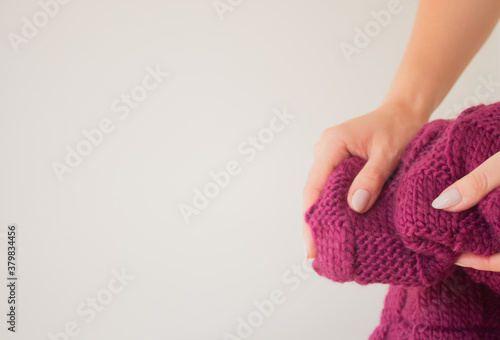 Knitted raspberry purple scarf in the hand of a young slender woman with a beautiful maicure. Knitted product close up mock up with copy space. Warm winter accessory