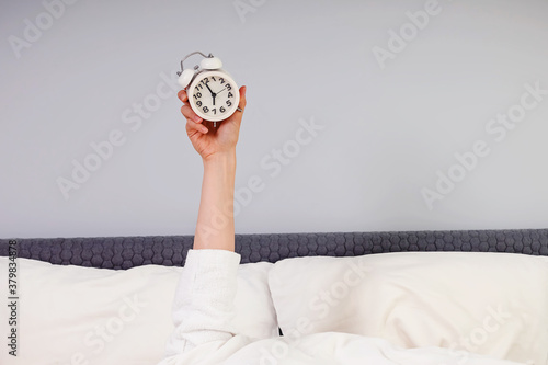 Hand stick out under the blanket showing alarm clock. photo