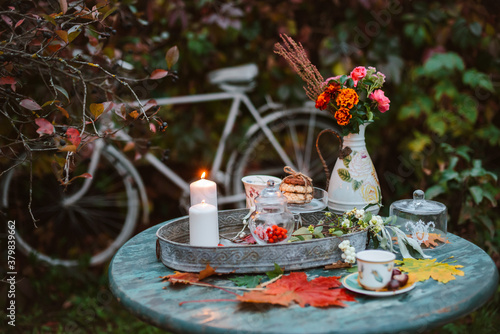 cozy patio. Autumn leaves lie on a wooden antique round table with crockery cups and cookies and candles.