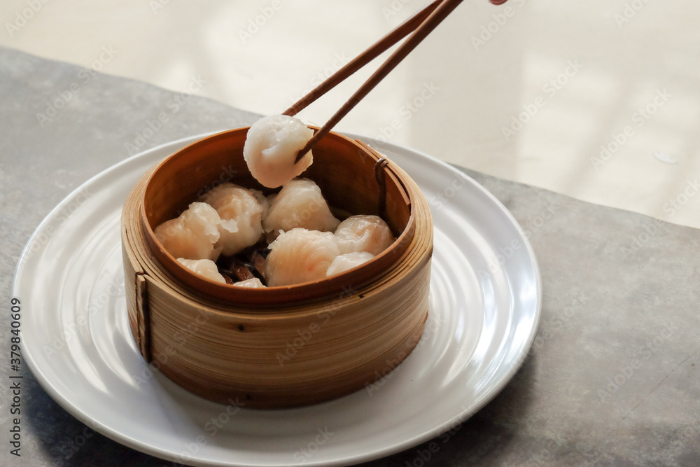 Asian steamed dish. Dim sum on a food shelves, various Chinese steamed dumpling in bamboo basket steamer in Chinese restaurants. with a chopstick Asian steamed dish. Dim sum on a food shelves, various Chinese steamed dumpling in bamboo basket steamer in Chinese restaurants. with a chopstick