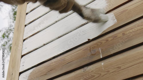 Hand close-up: painting a wooden wall handmade outdoors. A hand in a protective glove paints the Board with a brush in white. lifestyle, the concept of reconstruction. Side view, slow motion, 4K