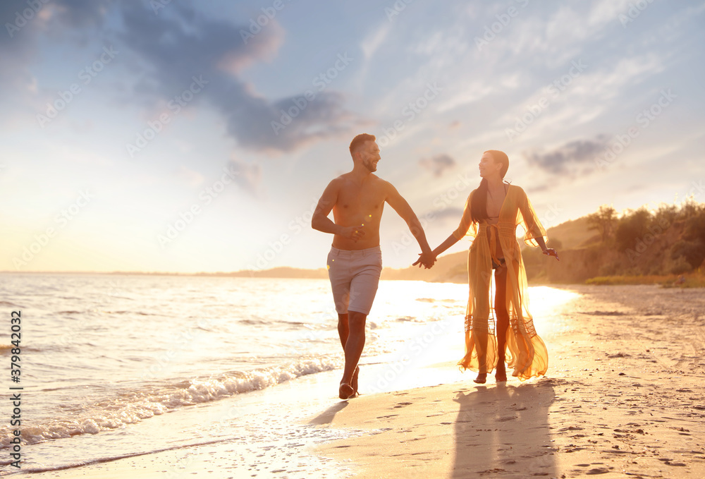 Happy young couple running together on beach at sunset Happy young couple running together on beach at sunset