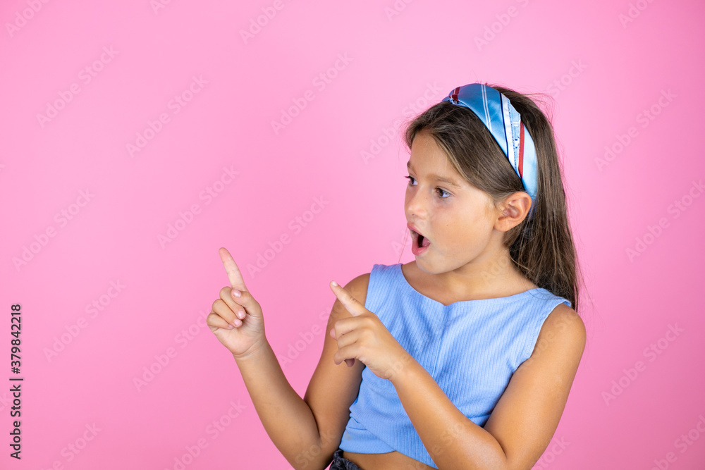Young beautiful child girl over isolated pink background surprised, looking and pointing side Young beautiful child girl over isolated pink background surprised, looking and pointing side