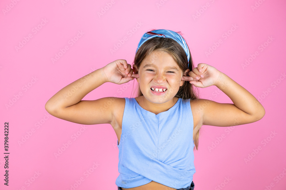 Young beautiful child girl over isolated pink background covering ears with fingers with annoyed expression for the noise of loud music. Deaf concept. Young beautiful child girl over isolated pink background covering ears with fingers with annoyed expression for the noise of loud music. Deaf concept.