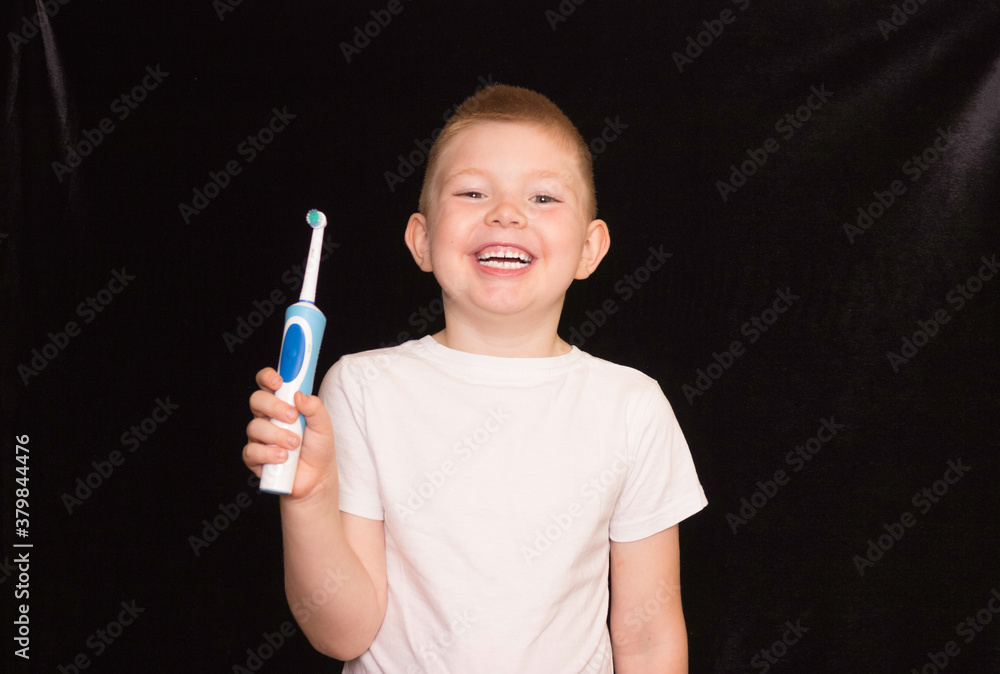 A boy brushes his teeth with an electric toothbrush on a black background. A boy brushes his teeth with an electric toothbrush on a black background.