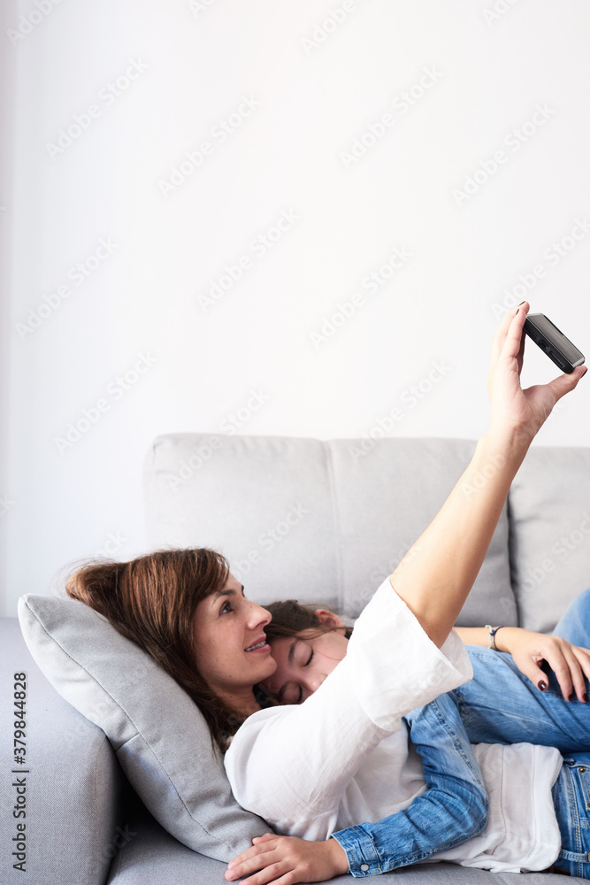 Smiling woman with kid taking selfie via mobile phone on sofa. Smiling woman with kid taking selfie via mobile phone on sofa.