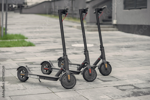 Three modern stylish black electric scooter are parked near big office centre. Electricity and eco friendly concept.