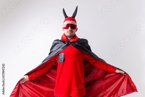Strange devilish man in sunglasses and black red halloween costume posing over white background.