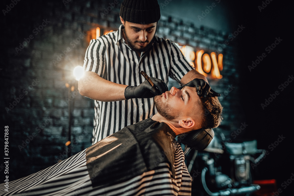 Stylish shaving and caring in professional dark saloon where barber cutting beard of his favourite client. Stylish shaving and caring in professional dark saloon where barber cutting beard of his favourite client.