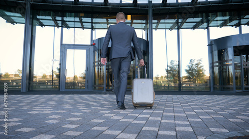 Businessman with baggage on the go. Caucasian businessman rolling luggage in lobby.