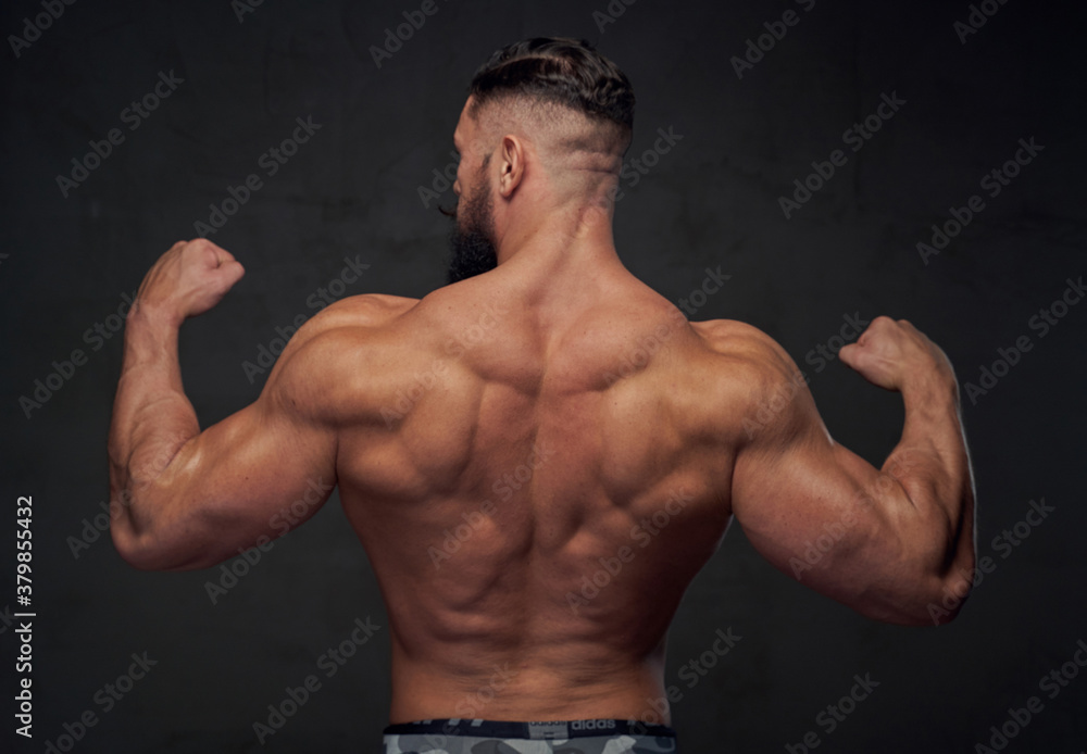 Brutal bodybuilder with strong hands and with modern hairstyle posing in gray background.