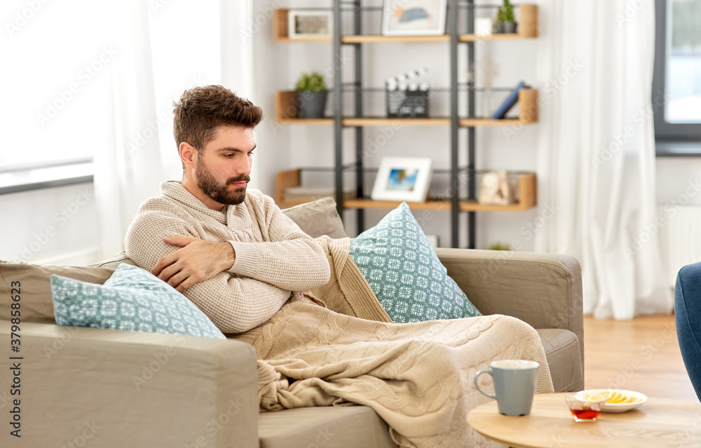 health, cold and people concept - sick young man in blanket with hot tea, lemon and honey on table at home health, cold and people concept - sick young man in blanket with hot tea, lemon and honey on table at home