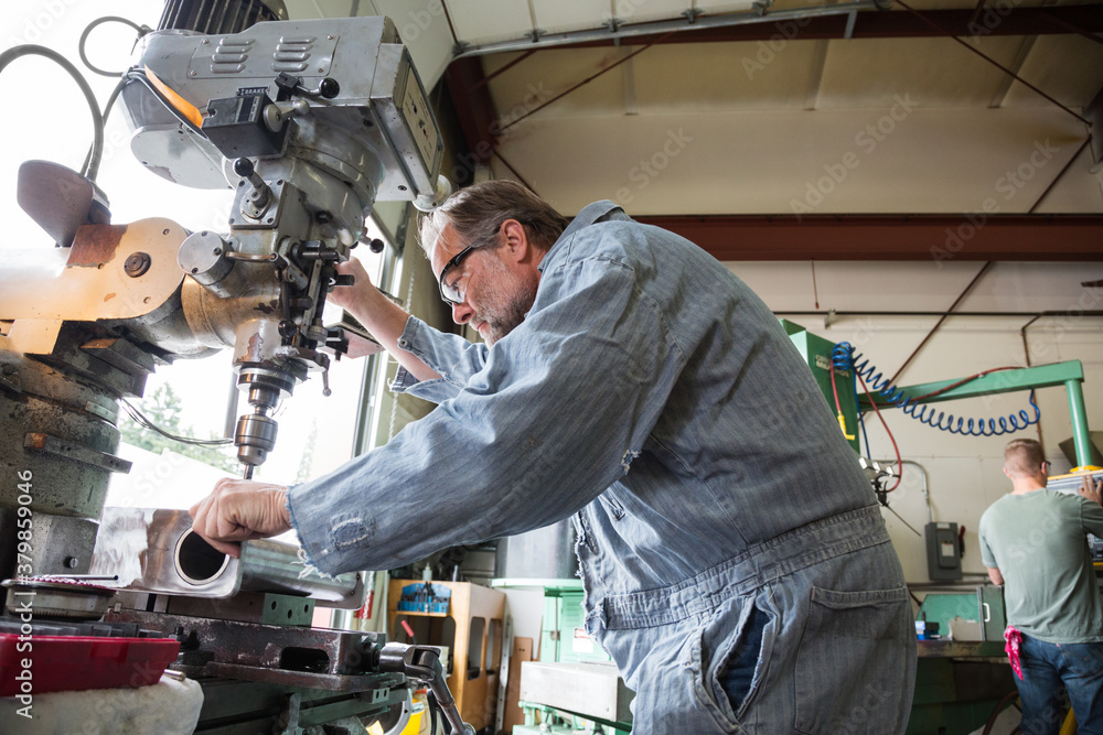Worker using drill press in factory