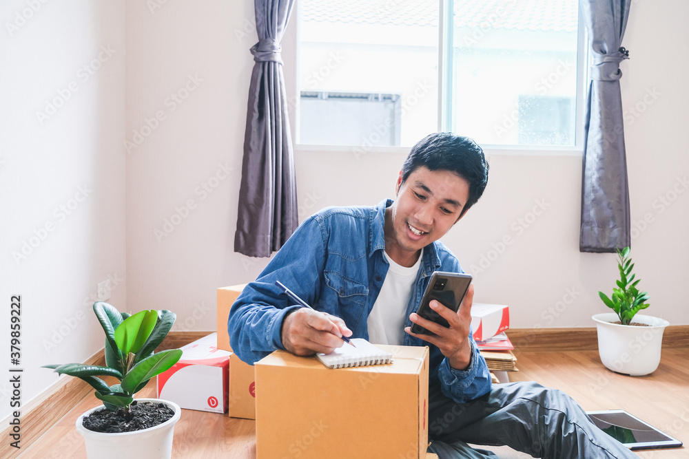 Asian man writing order product from customer calls to order he notes on notepad To prepare cargo or goods To transport to customers On days with new normol covid-19 Asian man writing order product from customer calls to order he notes on notepad To prepare cargo or goods To transport to customers On days with new normol covid-19