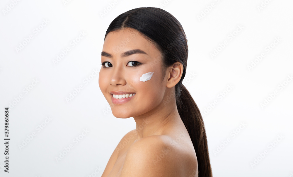 Face care concept. Asian girl applying cream on her cheek Face care concept. Asian girl applying cream on her cheek