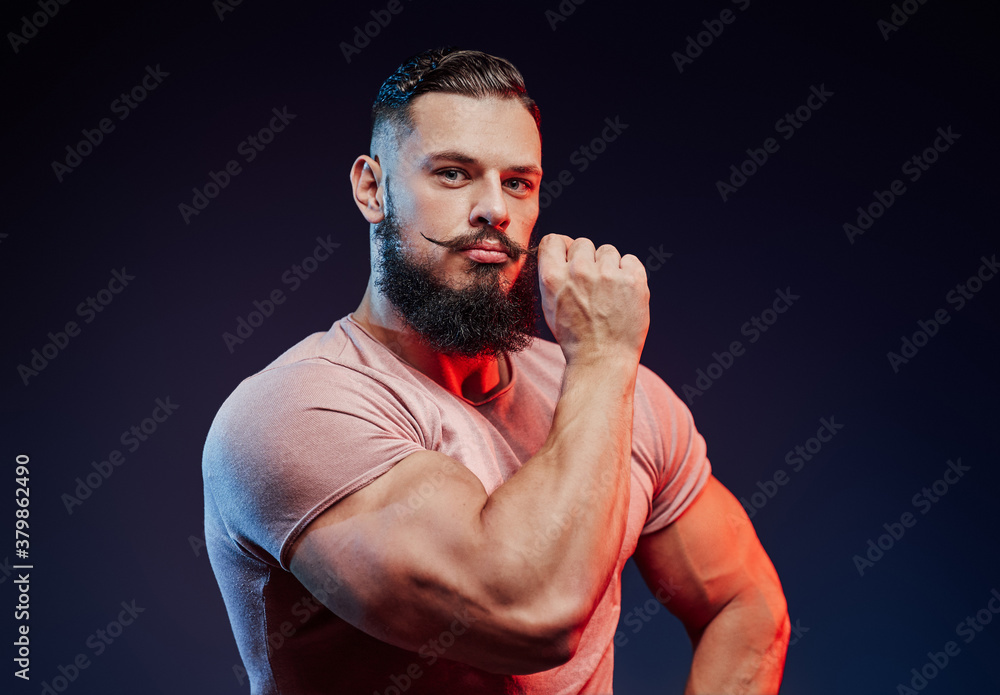 Fashionably dressed bodybuilder with stylish hairstyle posing touching his mustache in dark background.