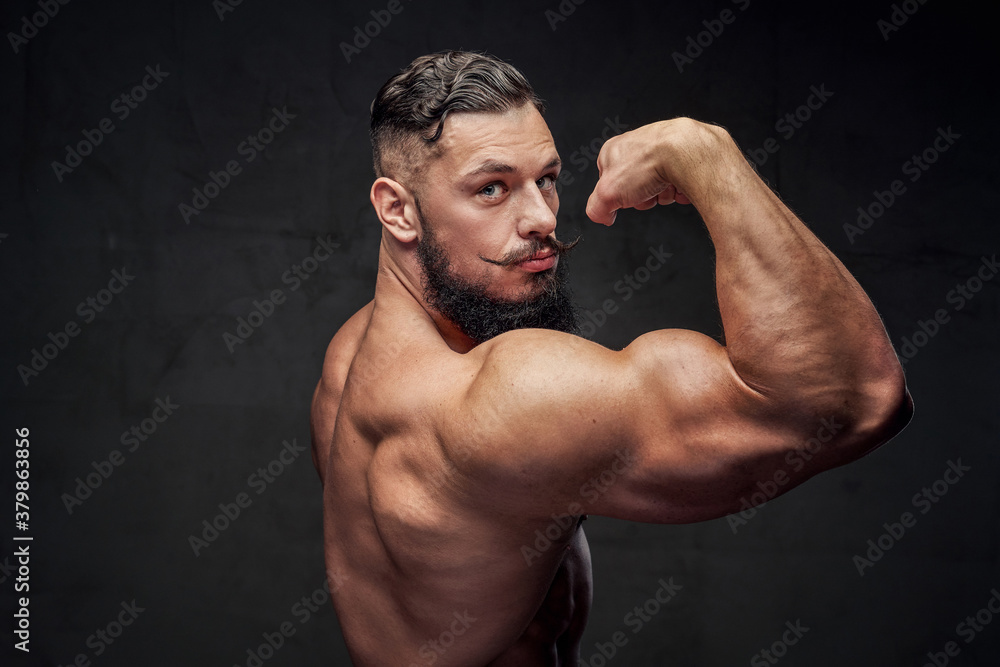 Handsome and muscular guy with beard and modern hairstyle posing in dark gray background.