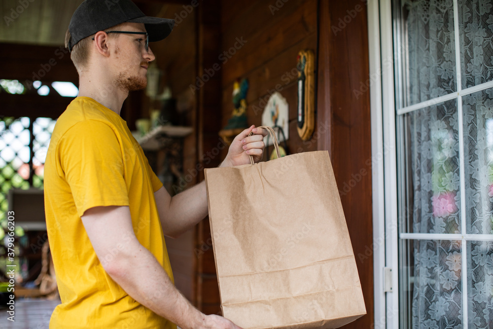Handsome young uniformed service courier stands at door of house with paper bags waiting for customer to come out. Stay home concept. disposable biodegradable bags, recycling and ecology concept
