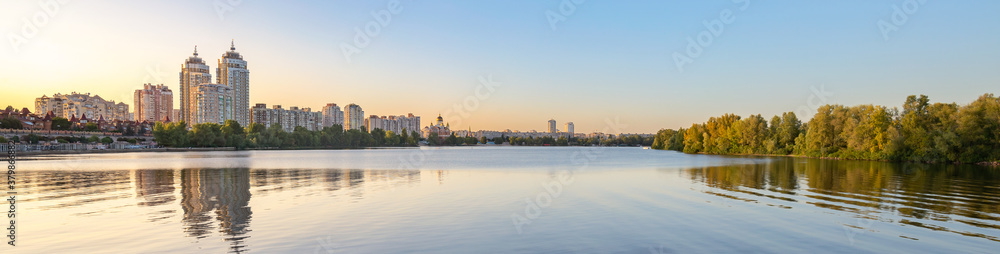 Panoramic view oth the high Obolon buildings near the Dnieper river in Kiev, Ukraine. Blue clear sky and reflection in the water.